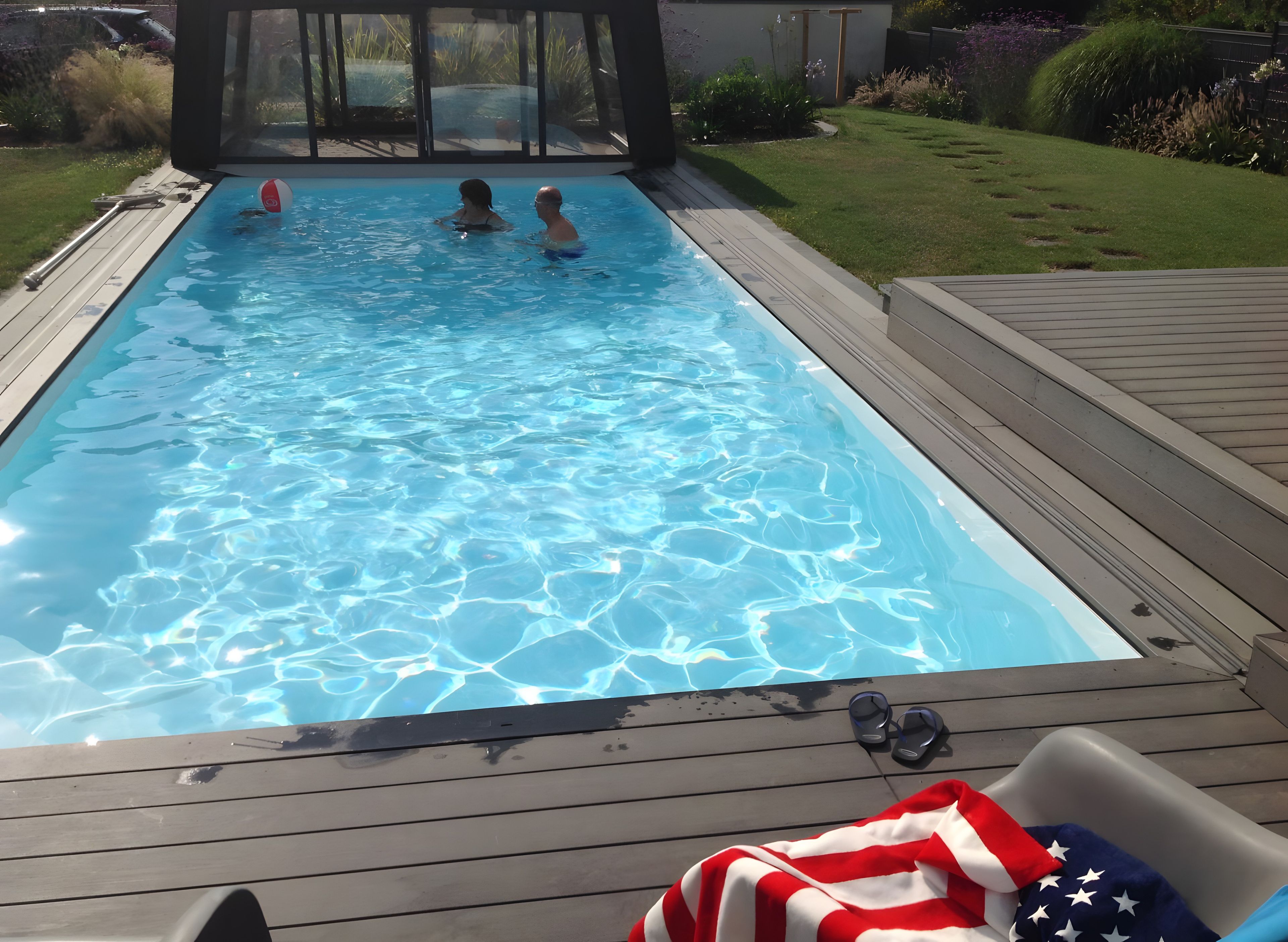 A swimming pool with clear water, surrounded by a wooden deck and a grassy area.