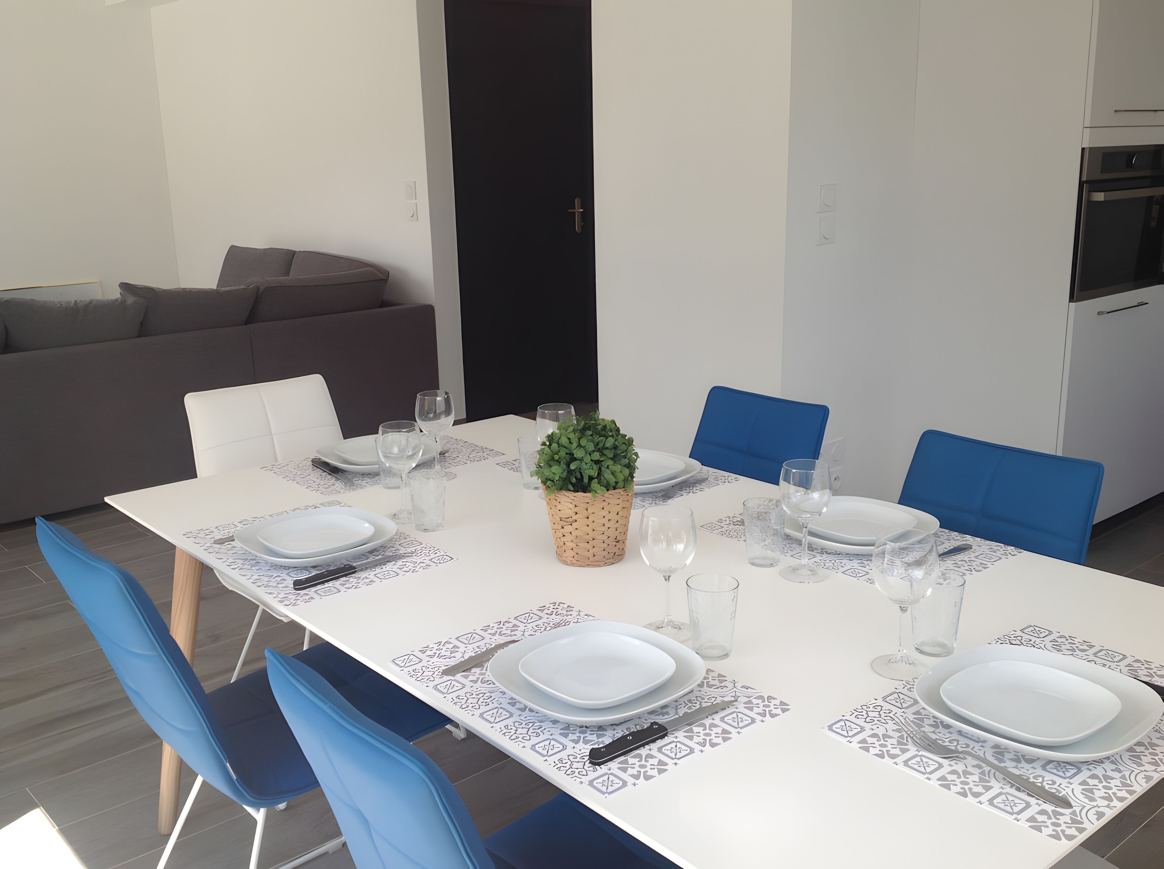 A dining area with a white table set for four, blue chairs, and a small potted plant.