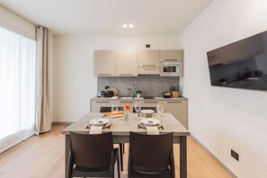 A modern kitchen with a dining area, featuring a flat-screen TV mounted on the wall, a built-in microwave, and a granite countertop. - Close To Everything 2 by Rent All Como (Como)