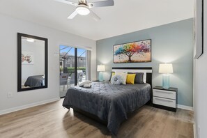 A bedroom with a bed, two bedside tables with lamps, a ceiling fan, a large mirror, and a painting on the wall. - Epic Providence Family Escape (Davenport)