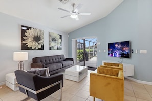 A modern living room with a grey sofa, a white coffee table, and a yellow armchair. There is a ceiling fan, a TV on the wall, and artwork above the sofa. - Epic Providence Family Escape (Davenport)