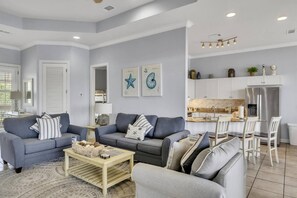 A modern living room with two sofas, a coffee table, and a dining area with chairs and a kitchen in the background. - 🌴Crystal Cove 2223 | Lake Views | Golf Cart⛳ (Miramar Beach)