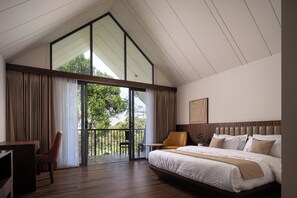 A modern bedroom with a large bed, a desk, and a chair. There is a balcony with a view of trees. - BREEZ WYNA (Kalpetta)