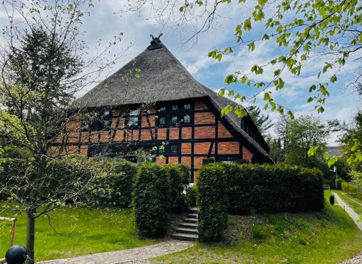 A traditional half-timbered house with a steeply pitched roof, surrounded by well-maintained hedges and a stone pathway leading to the entrance.