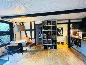 Une cuisine moderne avec un plancher en bois, un coin repas avec une table ronde et des chaises, et une bibliothèque contenant divers objets.