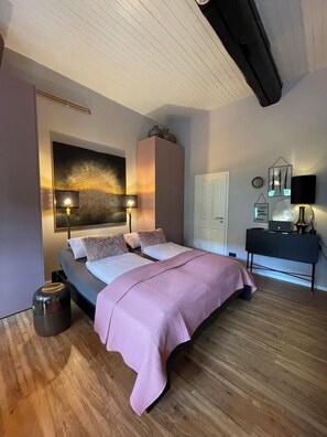 Une chambre à coucher comprenant un lit, des lampes de chevet, une commode et une œuvre d’art accrochée au mur.