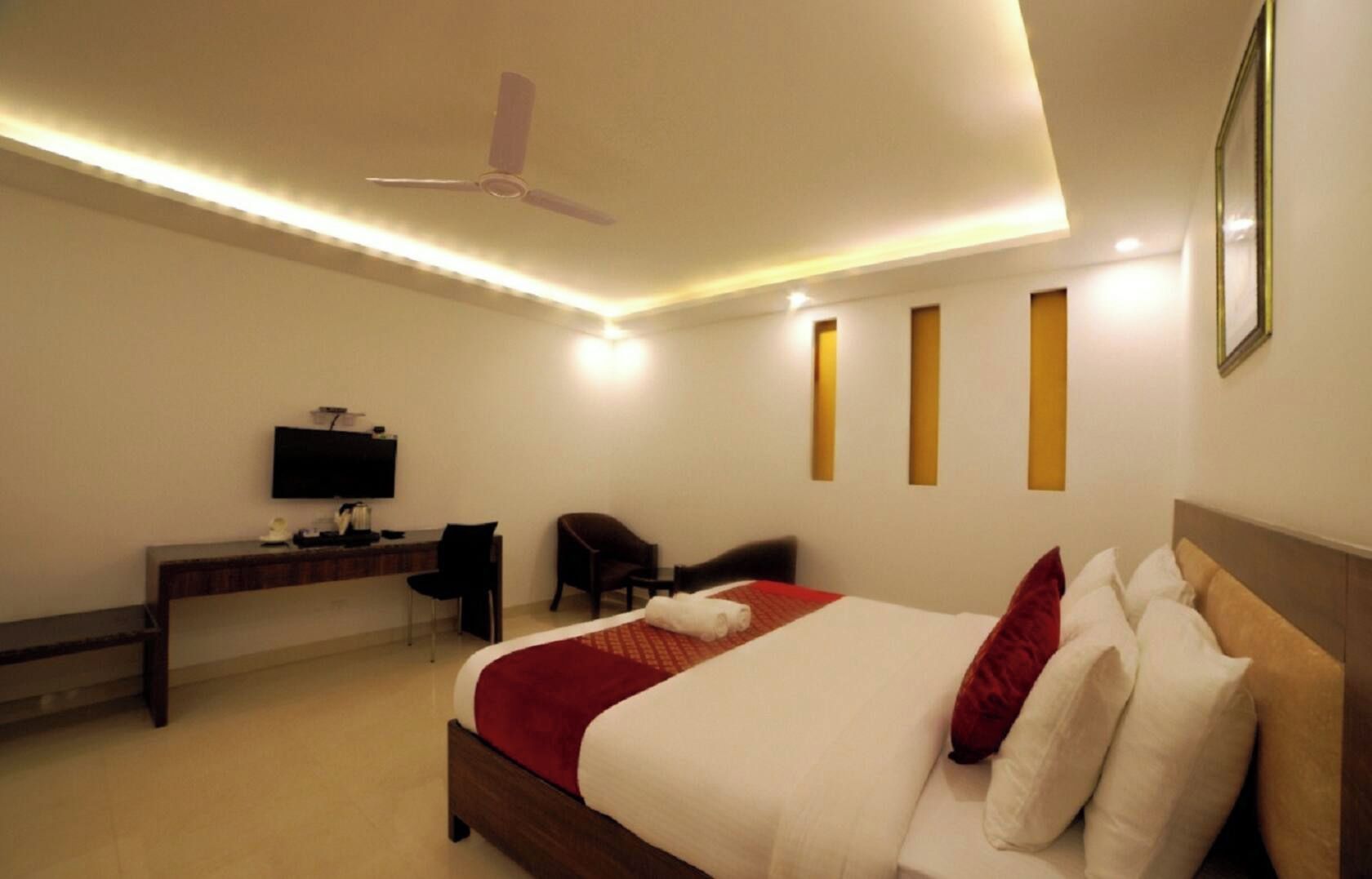 Ein Hotelzimmer mit Bett, Schreibtisch, Stuhl, Fernseher und Deckenventilator.