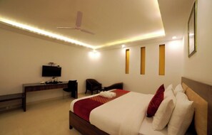 Une chambre d’hôtel équipée d’un lit, d’un bureau, d’une chaise, d’une télévision et d’un ventilateur de plafond.