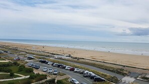 A parking lot adjacent to a beach with cars parked and a few people walking. - 2-Bedroom Apartment with Ocean View (Saint-Hilaire-de-Riez)