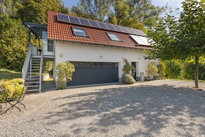Ein modernes Haus mit Kopfsteinpflasterauffahrt, einer Garage und Solaranlagen auf dem Dach.