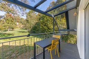 Een balkon met een tafel en stoel, met uitzicht op een tuin en bomen.