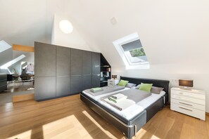 Ein modernes Schlafzimmer mit Dachfenster, einem Bett mit vielen Kissen, einem Nachttisch und einem Kleiderschrank.