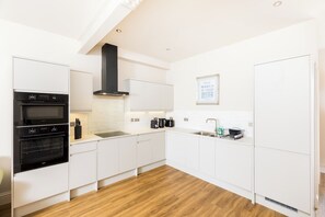 A modern kitchen with white cabinetry, a black range hood, and a stainless steel sink. - Stylish 1 Bedroom Apartment in the Heart of L Spa - Pass the Keys (Leamington Spa)