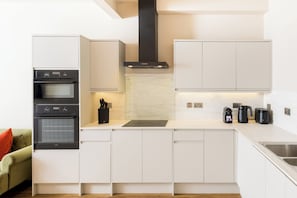 Een moderne keuken met witte kastjes, een inbouwoven, een afzuigkap en een aanrecht met een koffiezetapparaat en broodrooster.