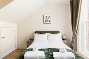 A hotel room with a bed, two bedside tables, a framed picture on the wall, and a window with curtains. - Stylish 1 Bedroom Apartment in the Heart of L Spa - Pass the Keys (Leamington Spa)