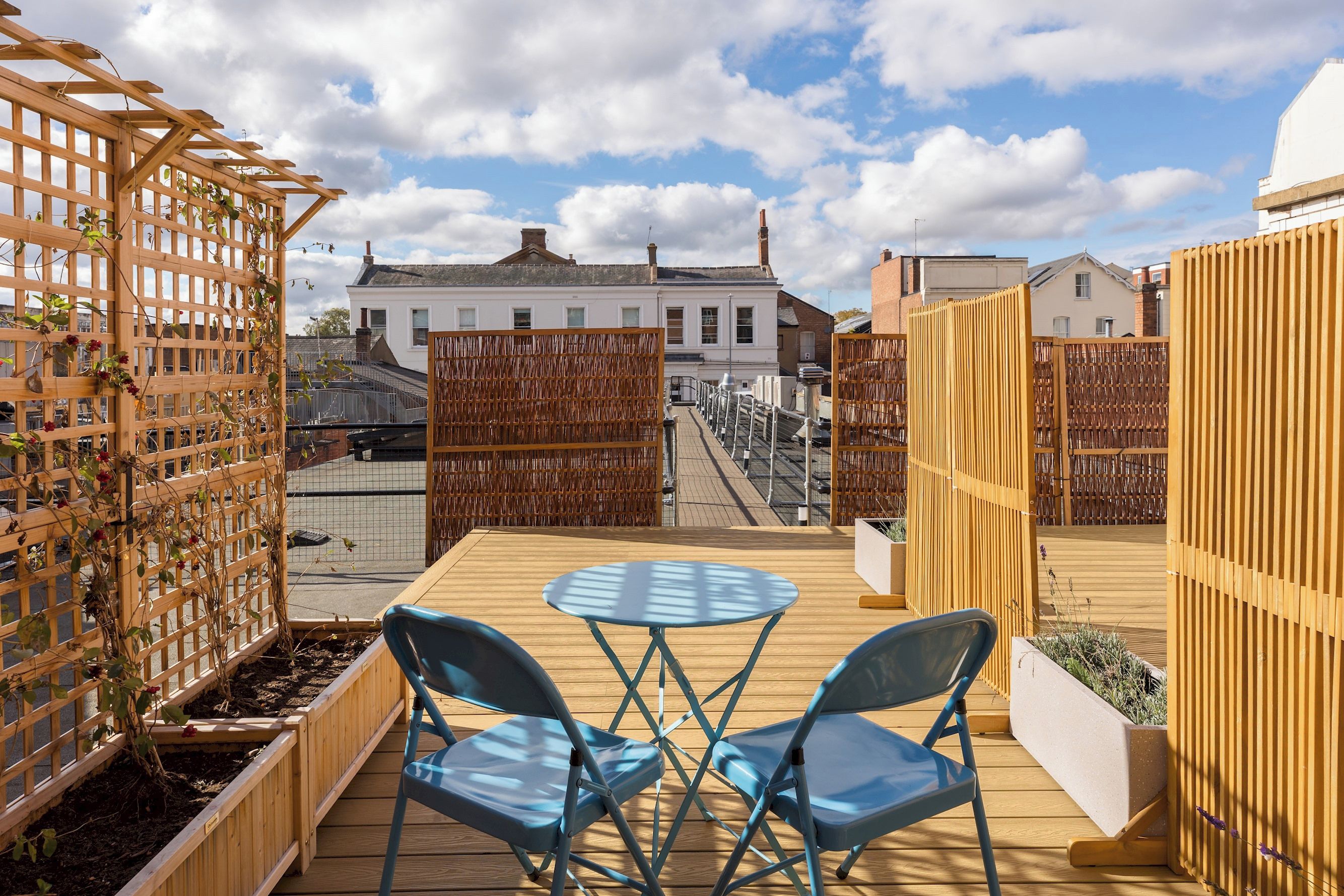 Une terrasse sur le toit avec une plateforme en bois, deux chaises bleues et une table.