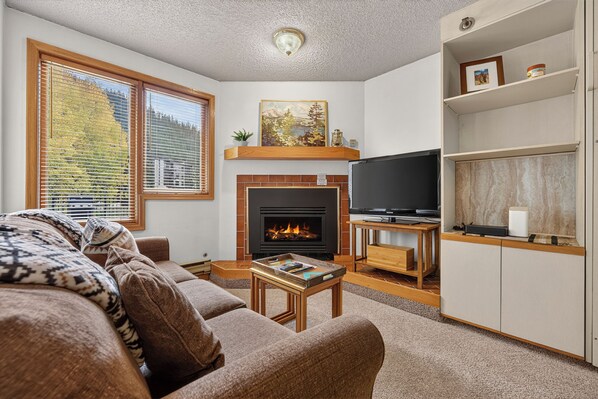 Unwind in your cozy living space, where a warm fireplace and mountain views through the windows create the perfect alpine retreat after a day of adventure. - Iron Horse Resort Unit C-1083 ski-in/out family condo rental (Winter Park)