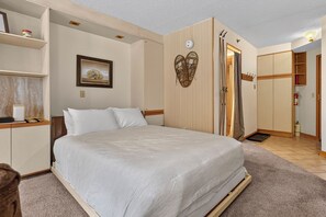 Een slaapkamer met een bed, een kledingkast, een plank met een foto en een deur met een kapstok.