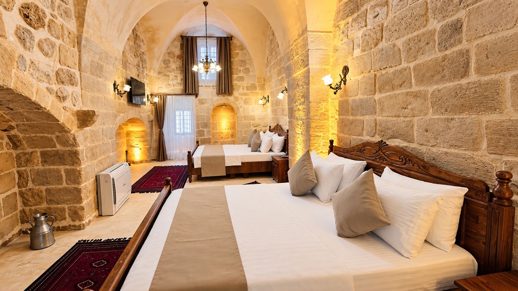 Habitación de hotel con paredes de piedra, una cama grande, cabecera de madera y un televisor fijado a la pared.
