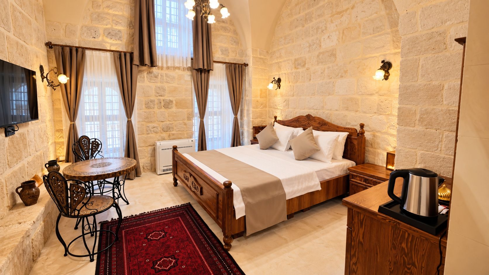 Une chambre d’hôtel avec un mur en pierre, un lit en bois, une table ronde et un tapis rouge.