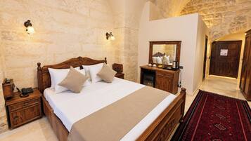 Habitación de hotel con una cama grande, mesitas de noche de madera, una mesilla, un espejo y una alfombra roja estampada.