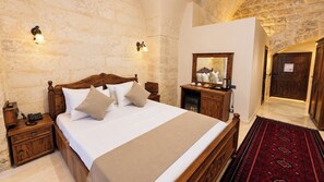 Habitación de hotel con una cama grande, mesitas de noche de madera, una mesilla, un espejo y una alfombra roja estampada.