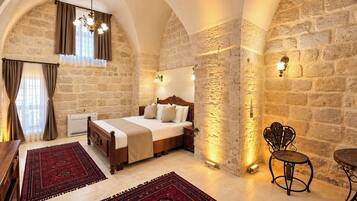 Un dormitorio con pared de piedra, cama de madera, alfombra roja y una silla de metal.