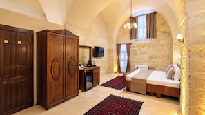 Un dormitorio con cama, armario de madera, escritorio con televisor y pared de piedra.