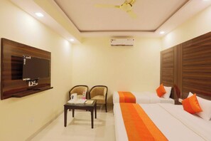 Une chambre d’hôtel comprenant un lit, deux chaises, une petite table, un téléviseur fixé au mur et un appareil de climatisation.