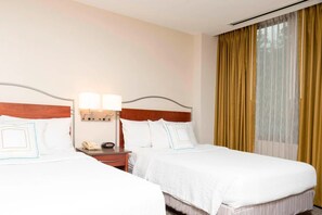 Ein Hotelzimmer mit zwei Betten, einem Nachttisch mit Lampe, einem Telefon und einem Fenster mit Vorhängen.