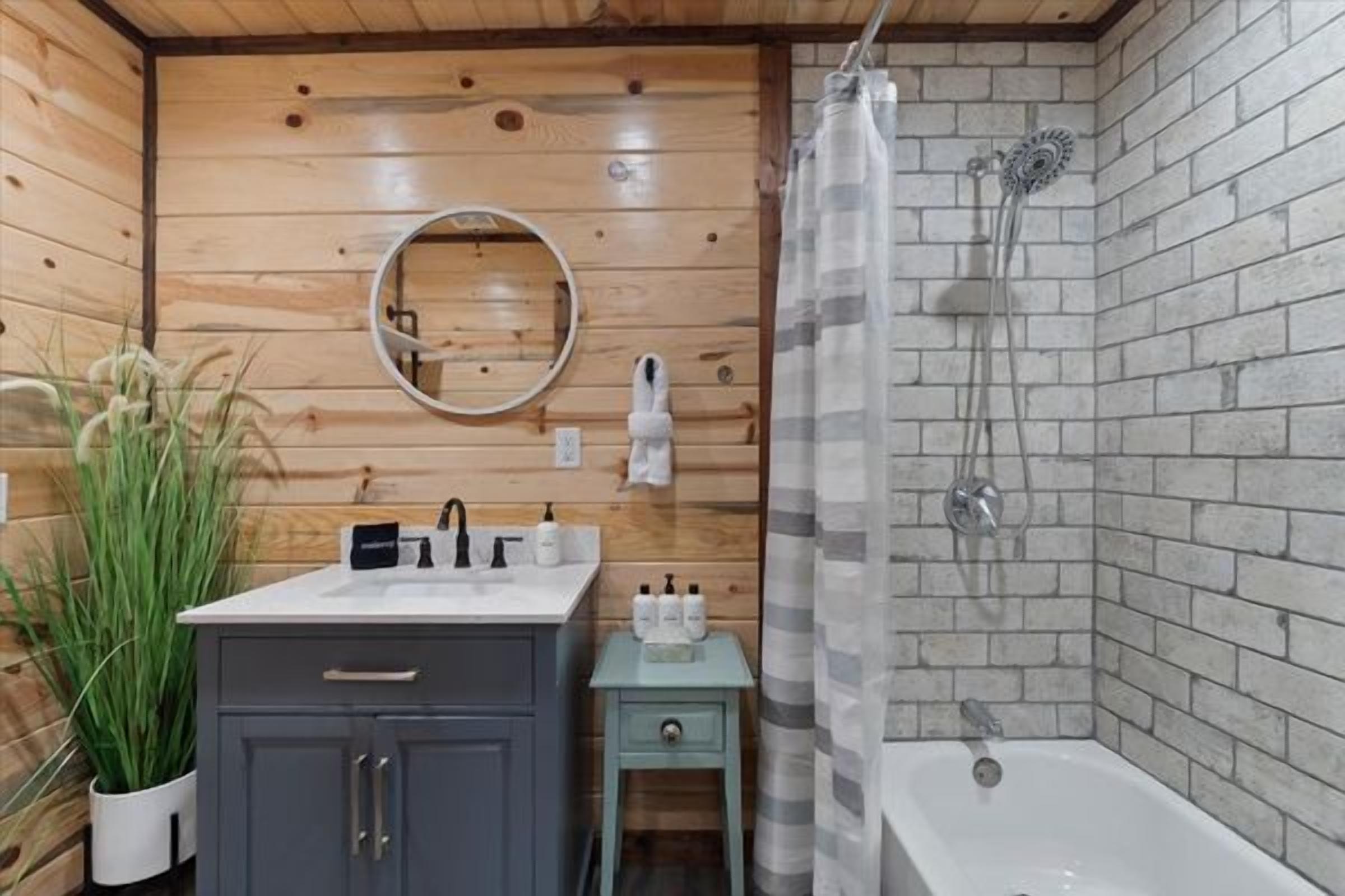 A bathroom with a wooden vanity, a sink, a mirror, a shower with a glass door, and a small table with toiletries.