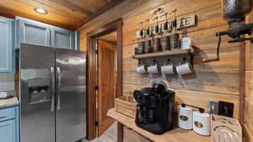 A kitchen with a stainless steel refrigerator, wooden cabinets, a coffee machine, and a shelf with jars and utensils.