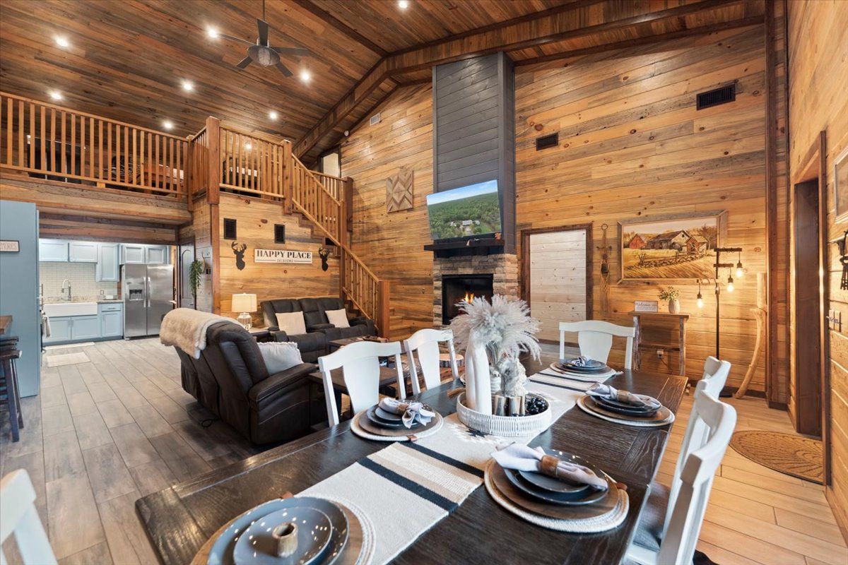 A spacious living area with a fireplace, a dining table set for six, and a kitchen in the background.