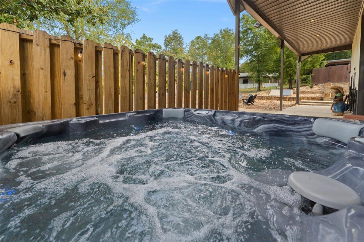 A hot tub with a wooden fence in the background, a covered patio area, and a stone structure.