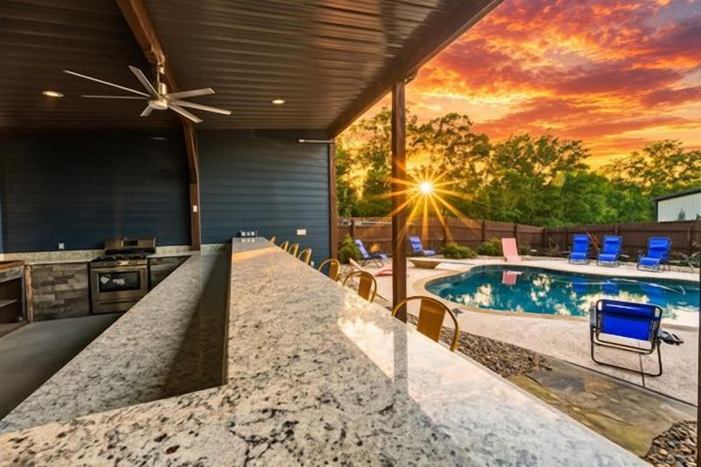 An outdoor bar area with a pool, lounge chairs, and a sunset view.