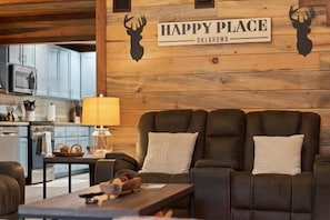 A cozy living room with a dark leather sofa, a coffee table, and a kitchen in the background. - Heated Pool | 14-Acre Ranch | Lake & Hot Tub (Broken Bow)
