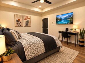 Un dormitorio con una cama, un escritorio, una silla, un televisor y obras de arte en la pared.