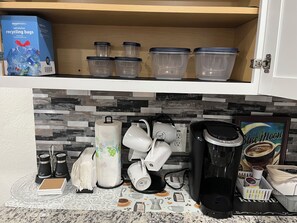 Une cuisine équipée d’une machine à café, de salières et de poivrières, d’un porte-essuie-tout et d’une boîte de sacs de recyclage de la marque Amazon Basics.