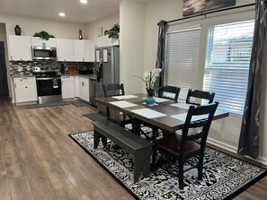 Una cocina moderna con armarios blancos, electrodomésticos de acero inoxidable y un comedor con mesa y sillas de madera.