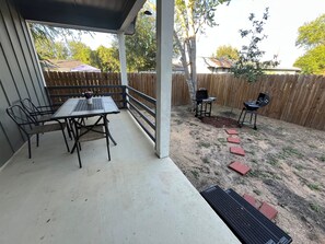 Un patio cubierto con una mesa, sillas, una parrilla y una cerca de madera.