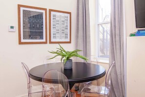 A dining area with a round table, clear chairs, a potted plant, and two framed artworks on the wall. - Essential Boston Home, Near South End (Boston)