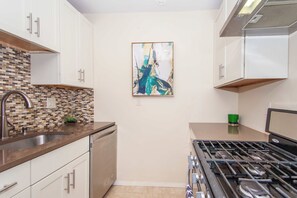 A kitchen with white cabinets, a tiled backsplash, a stove, and a painting on the wall. - Essential Boston Home, Near South End (Boston)