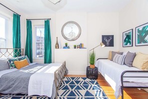 A modern bedroom with two beds, a geometric patterned rug, a round mirror, and wall art. - Essential Boston Home, Near South End (Boston)