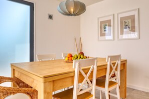 A dining area with a wooden table, white chairs, a fruit bowl, and two framed pictures on the wall. - Blue House, a Home in Madeira (Ponta do Sol)