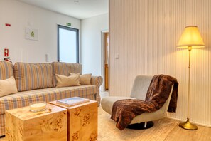 A hotel room with a striped sofa, a wooden side table, a reading lamp, and a chair with a throw blanket. - Blue House, a Home in Madeira (Ponta do Sol)