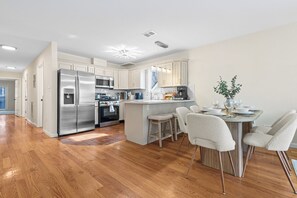 A modern kitchen with stainless steel appliances, a central island with bar stools, and wooden flooring. - Upscale Cozy Home Private Deck American Dream Metlife near NYC (Jersey City)