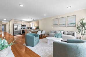 Una sala de estar moderna con un sofá, sillones, una mesa de centro y una cocina al fondo.