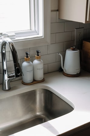 A kitchen with a stainless steel sink, a faucet, two bottles of dish soap, and a kettle on the countertop. - Upscale Cozy Home Private Deck American Dream Metlife near NYC (Jersey City)