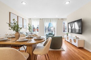 Un comedor moderno con una mesa de madera preparada para cuatro personas, un sofá y un televisor montado en la pared.