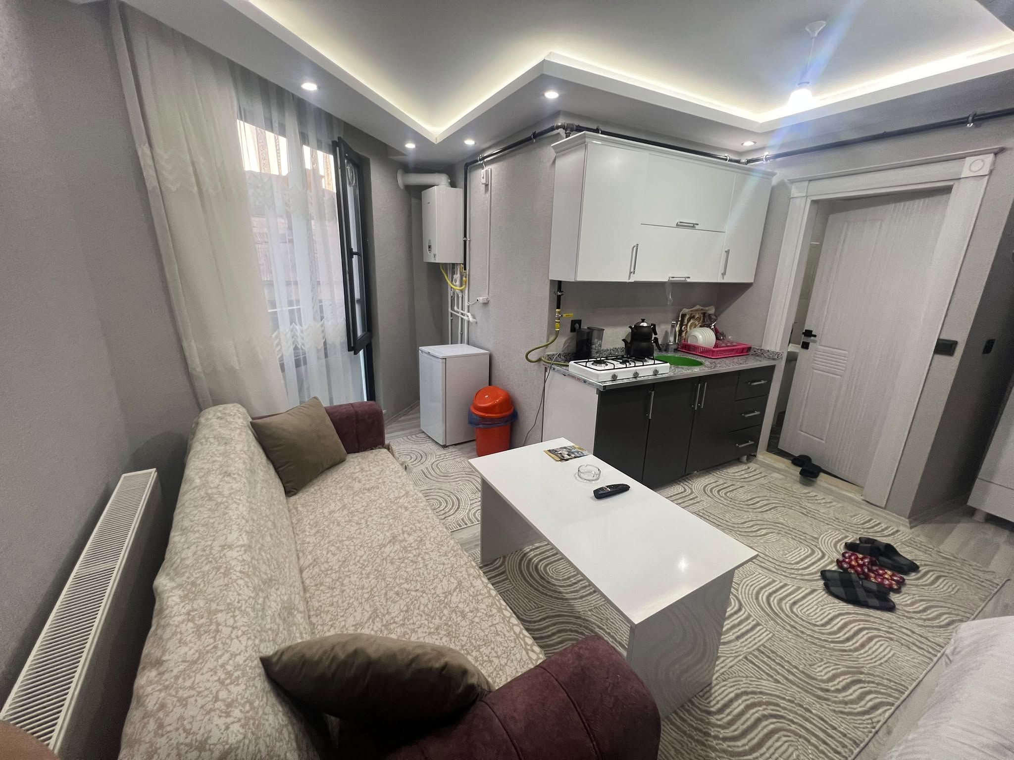 Een moderne woonkamer met een bank, een salontafel en een keuken met kastjes en een gasfornuis.